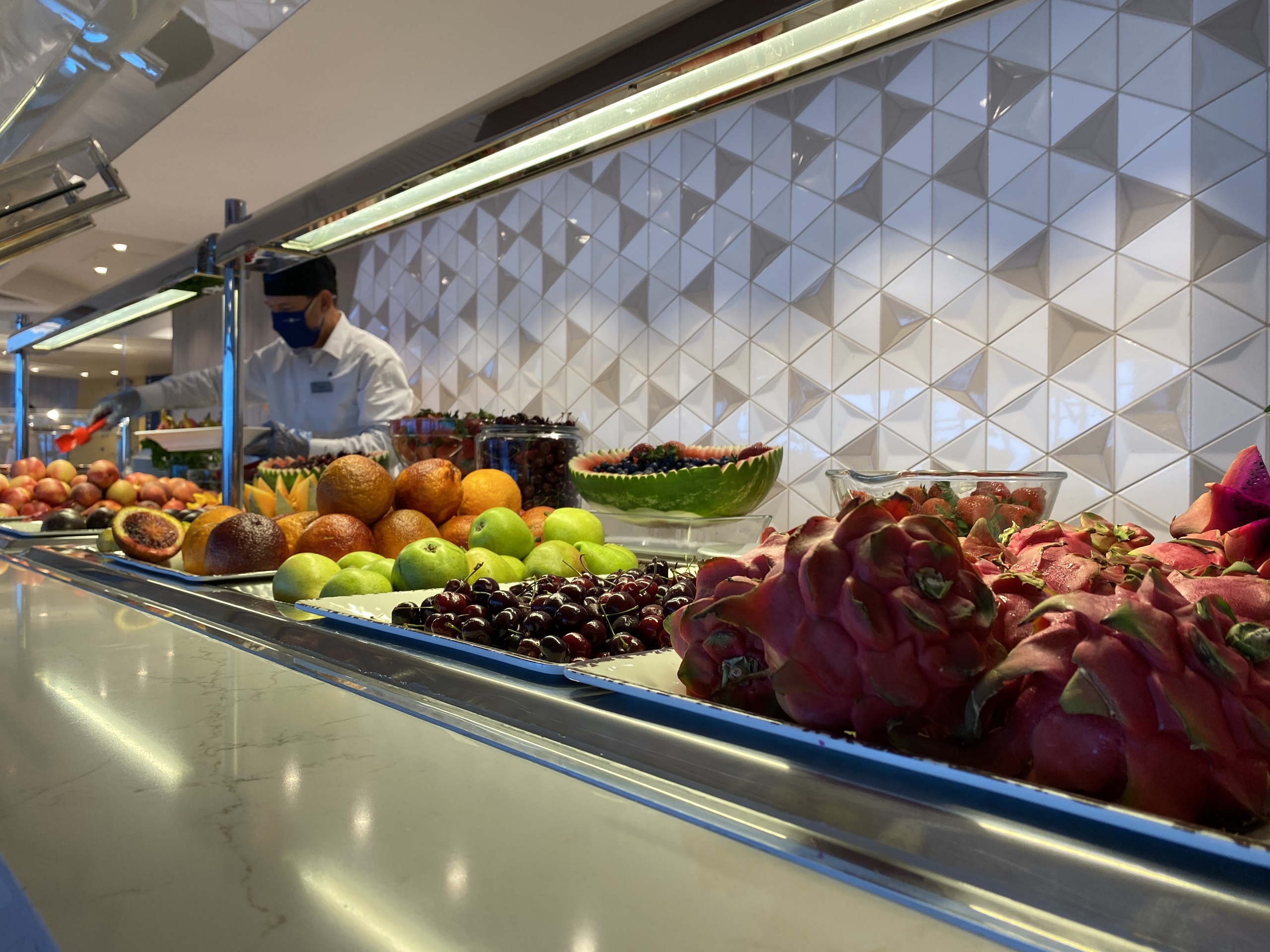 A crew member restocks fruit at a buffet counter, where food is no longer self-serve.