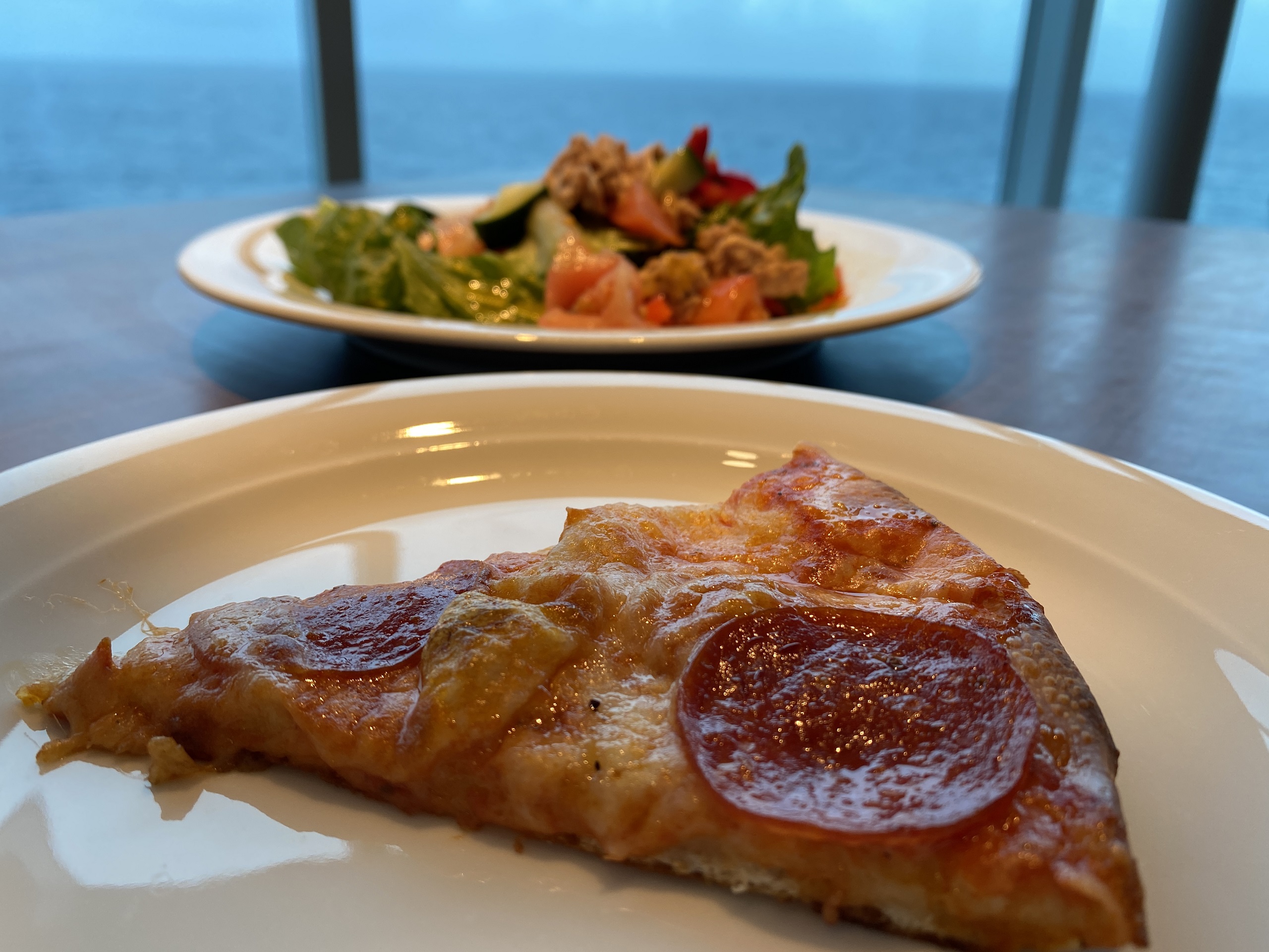 Pizza and salad in front of a window in the buffet with the ocean in the background