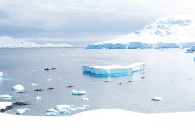 people kayaking by a large iceberg