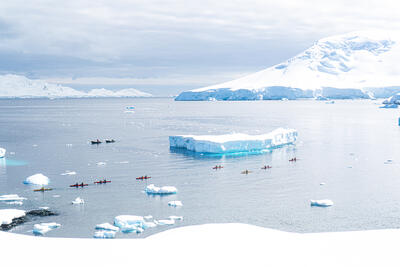 people kayaking by a large iceberg