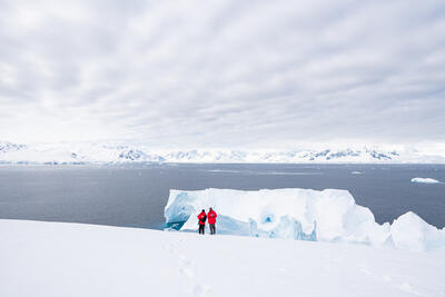 two travelers standing in front of a large iceberg