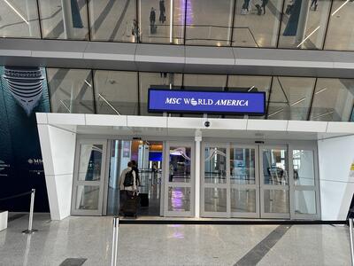 The entryway of a cruise terminal with a walkway, glass doors and an LED sign that says "MSC World America"