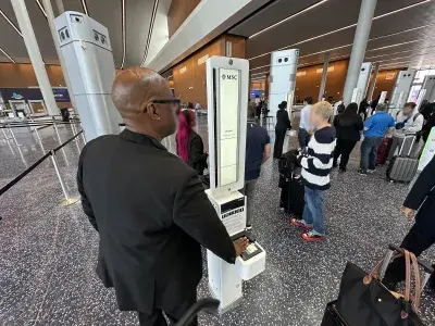 A port agent helps passengers scan their passports at a cruise terminal's biometric kiosks
