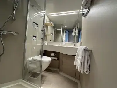 A cruise ship bathroom with a fiberglass shower, toilet, sink, vanity and towels