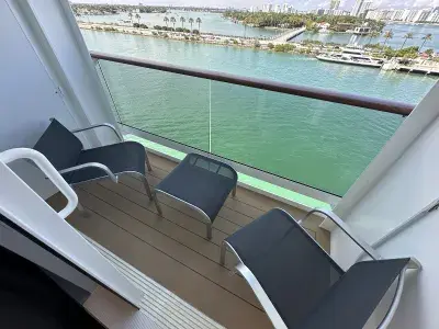 A cruise ship balcony with two mesh chairs and a small stool overlooking green water in Miami
