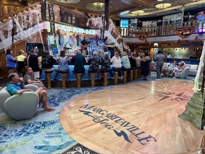 An atrium with a wooden dance floor and cruisers sitting around a bar facing a man playing guitar on stage