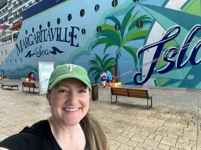 A selfie of a woman in front of a cruise ship where part of "Margaritaville at Sea Islander" is visible on the hull