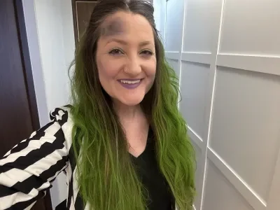 A woman with green hair dressed as Beetlejuice in a black-and-white-striped suit