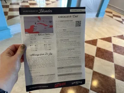 A hand holding a copy of a daily schedule from Margaritaville at Sea's Islander cruise ship