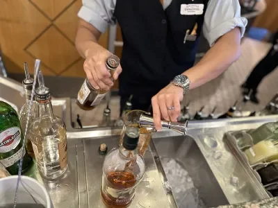 The hands of a bartender mixing a cocktail on a stainless steel counter
