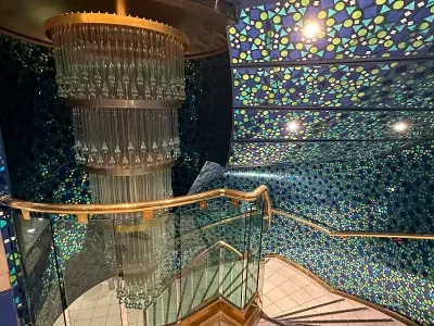 The mosaic-tiled entrance to the Coral Reef Lounge on Margaritaville's Islander cruise ship, complete with a spiral staircase and two-deck chandelier with glass teardrops hanging from it