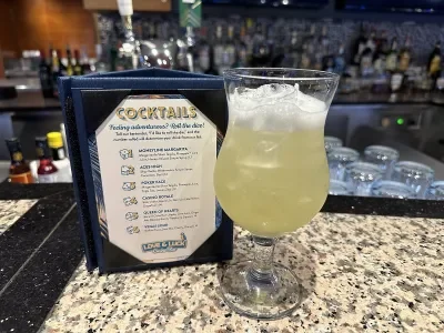 A cocktail menu next to a mixed drink on top of a bar