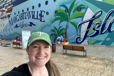 A selfie of a woman in front of a cruise ship where part of "Margaritaville at Sea Islander" is visible on the hull